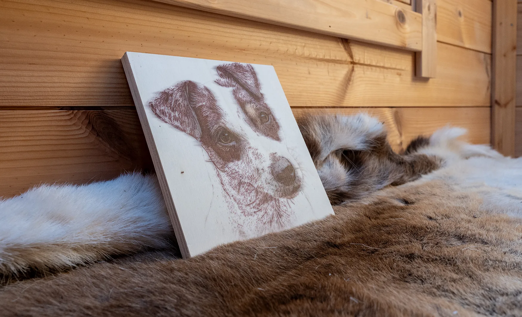 Wooden board with a wood burn style portrait of a Jack Russell Terrier, leaning against a panelled wall on top of a soft fur rug.